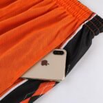 Orange black reversible basketball shorts with deep pocket holding iPhone size demonstration