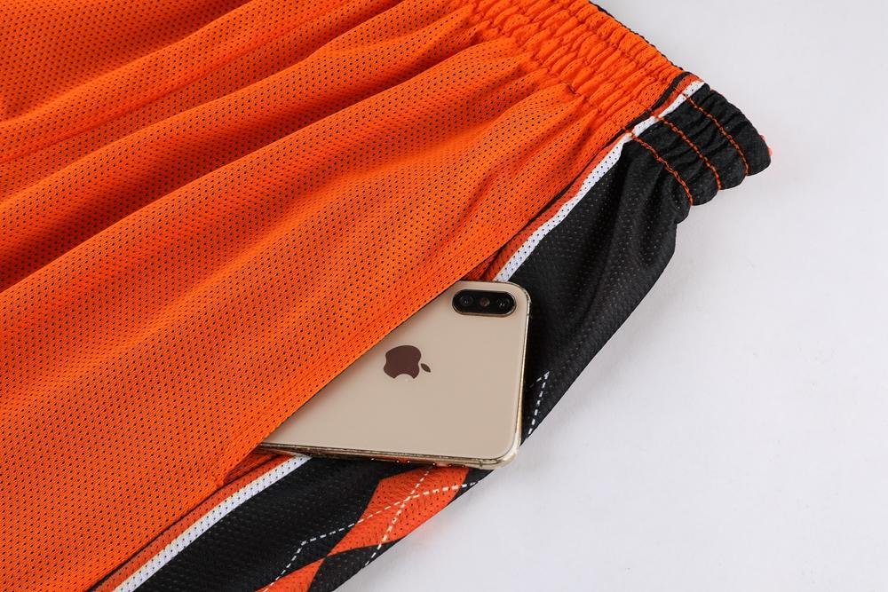 Orange black reversible basketball shorts with deep pocket holding iPhone size demonstration