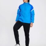 Man wearing blue hooded soccer windbreaker with black pants and football under foot