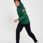 Man wearing green and yellow soccer windbreaker with black pants and football