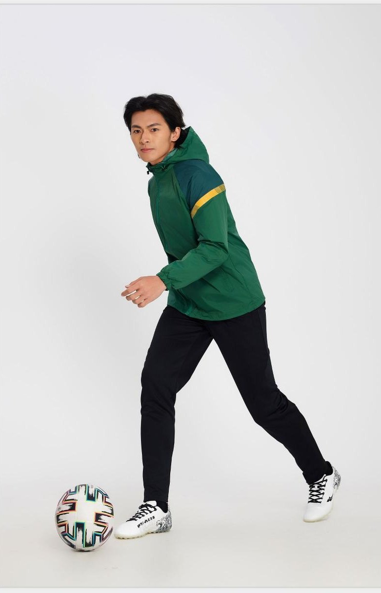 Man wearing green and yellow soccer windbreaker with black pants and football