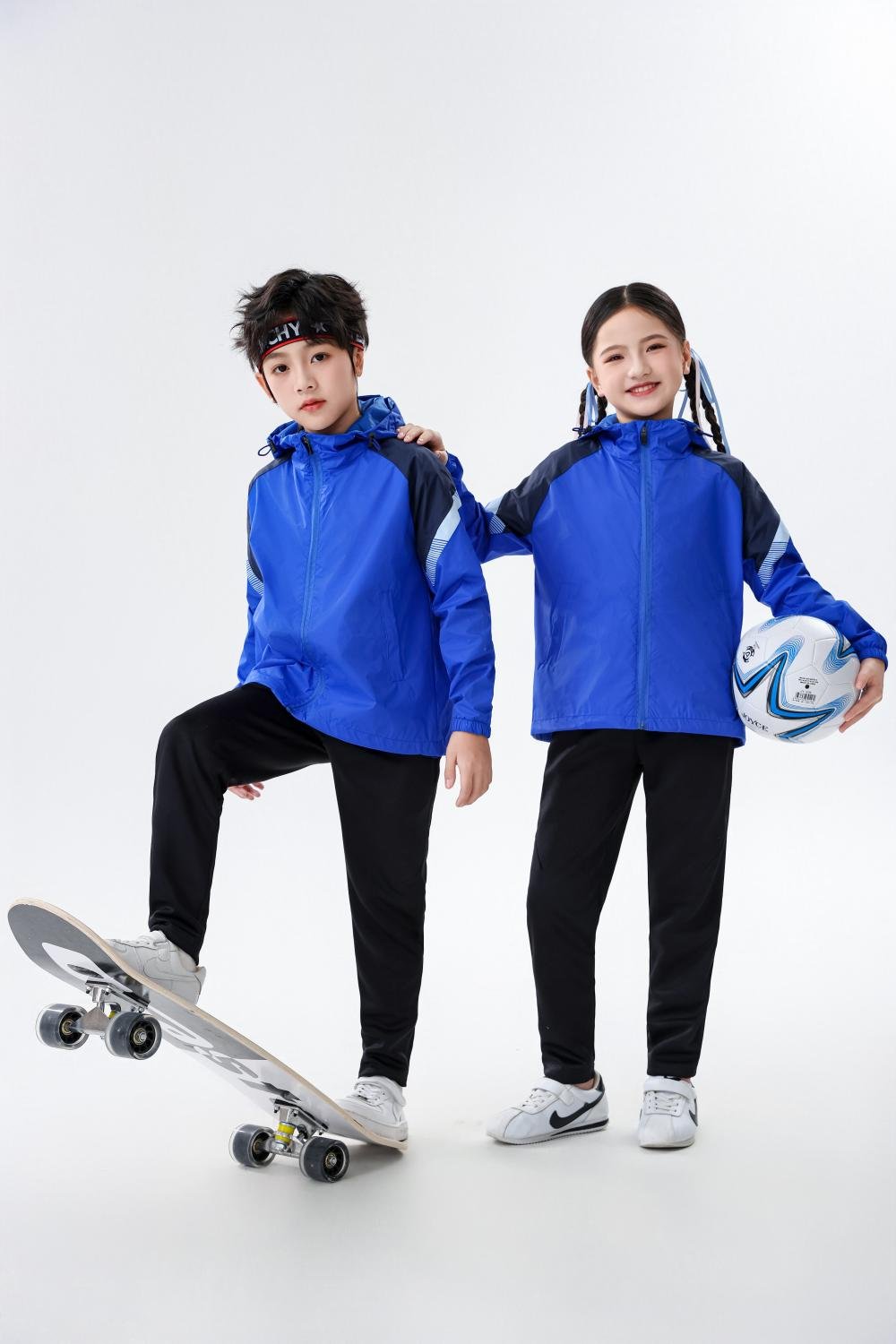 Boy and girl in blue soccer windbreakers, boy with skateboard, girl holding football