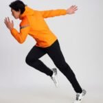 Man in orange soccer windbreaker performing dynamic running pose