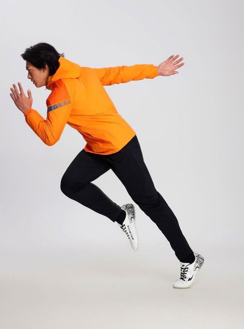 Man in orange soccer windbreaker performing dynamic running pose
