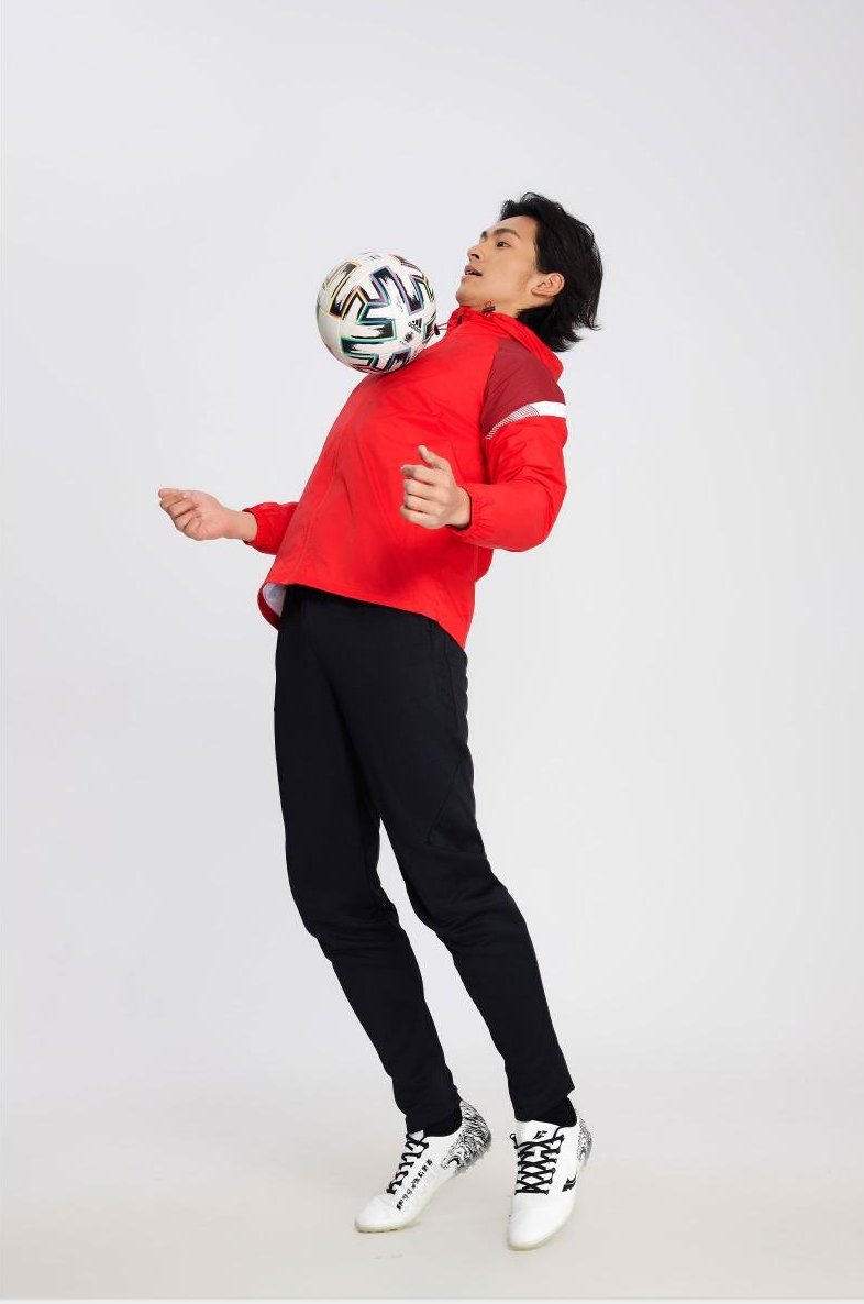 Man in red soccer windbreaker balancing football on head in dynamic pose