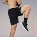 Side view of wholesale black training shorts on a model, highlighting the practical side zipper pocket and stretch fabric for custom sportswear production.