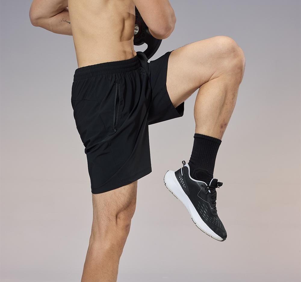 Side view of wholesale black training shorts on a model, highlighting the practical side zipper pocket and stretch fabric for custom sportswear production.