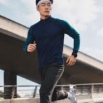 Male athlete running outdoors wearing a wholesale soccer full-zip training suit in navy and teal.