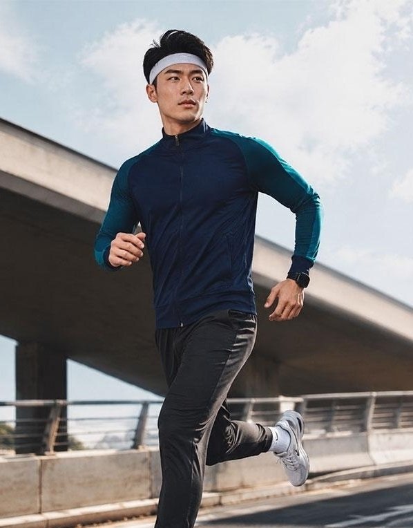 Male athlete running outdoors wearing a wholesale soccer full-zip training suit in navy and teal.