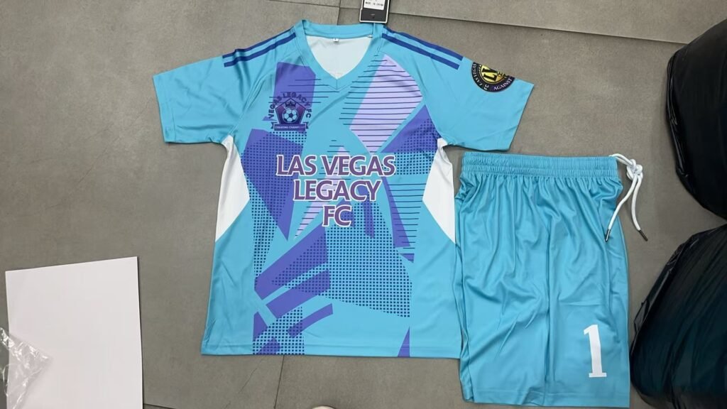 OEM custom light blue and purple abstract sublimation soccer jersey front view, featuring heat transfer team logo and sponsor, with ribbed V-neck and drawstring shorts.