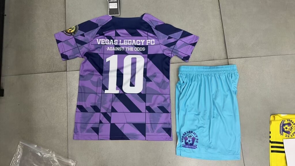 Custom purple and navy geometric sublimation soccer jersey front view with heat transfer team name, paired with light blue shorts for small batch OEM.