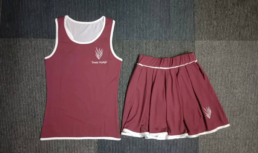 Flat lay shot of custom maroon 2-piece women's tennis set with racerback tank top and pleated skort made of 190GSM milk silk fabric.