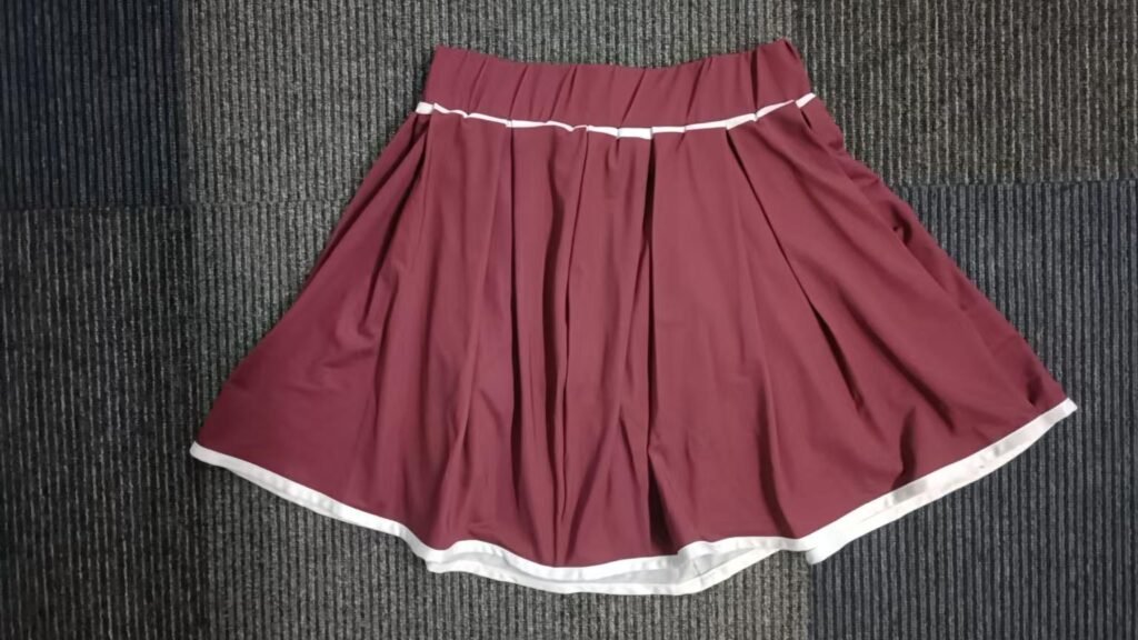 Front view of custom maroon pleated tennis skirt with white contrast hem and embroidered logo.