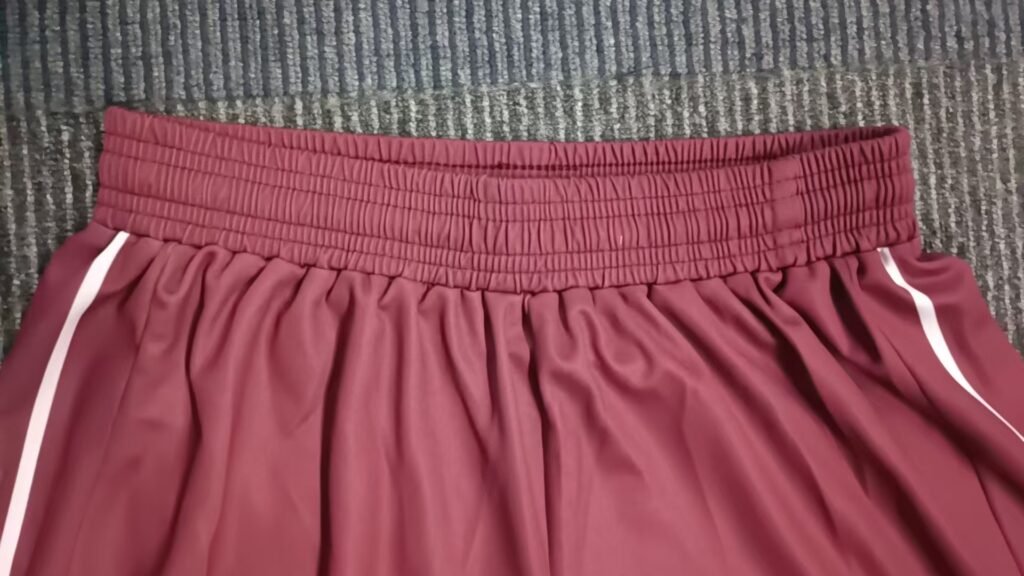 Close-up of flexible elastic waistband with multi-row stitching on maroon custom performance tennis shorts.