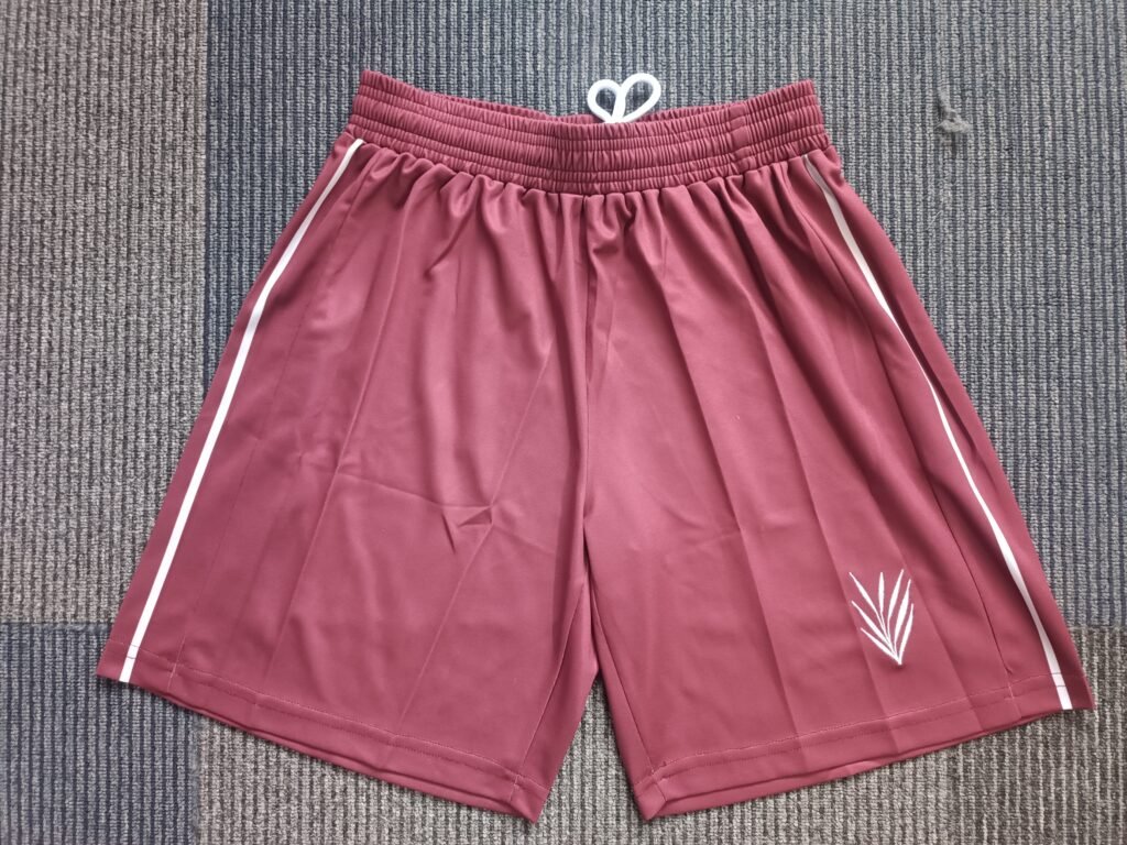 Flat-lay view of matching maroon athletic tennis shorts with white drawstrings, side seam stripes, and embroidered logo on left leg.