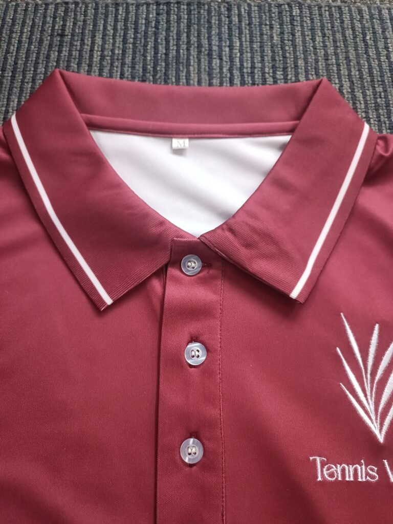 Close-up of maroon custom tennis polo shirt collar featuring white striped ribbing, 3-button placket, and white embroidered logo on breathable pique fabric.