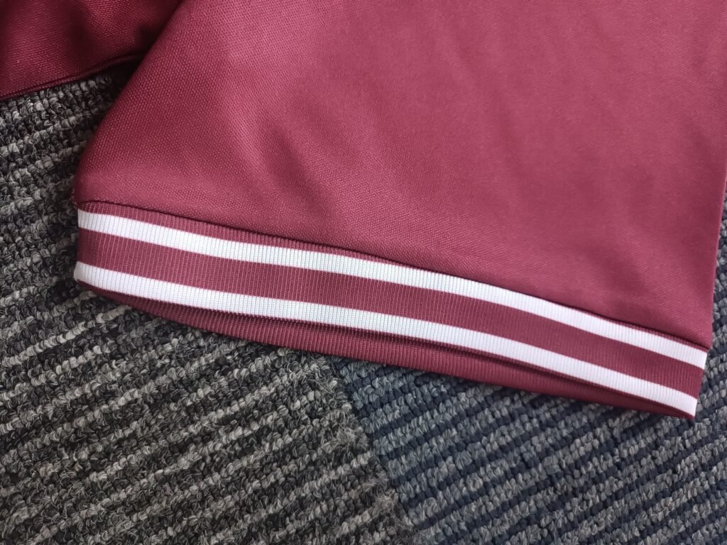 Macro shot of custom dark maroon sleeve cuff with double white accent stripes on lightweight performance polyester fabric.