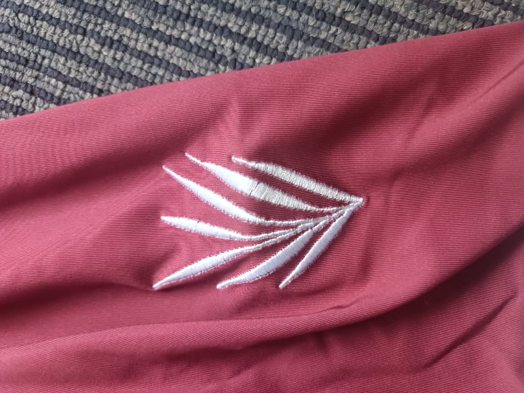 Detailed view of custom embroidered feather leaf icon on maroon activewear garment.